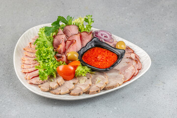 Assorted smoked meat slices with lettuce, onions, olives, tomatoes, and spicy sauce on a white plate with copy space