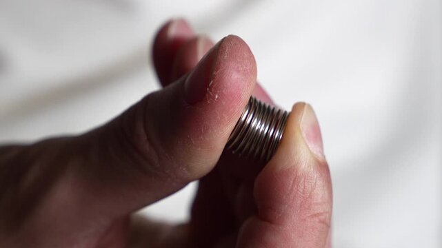 A man squeezes a tight, strong spring with his thumb.
A close-up of a metal spring in a man's hands.
Spring, metal, part, bending