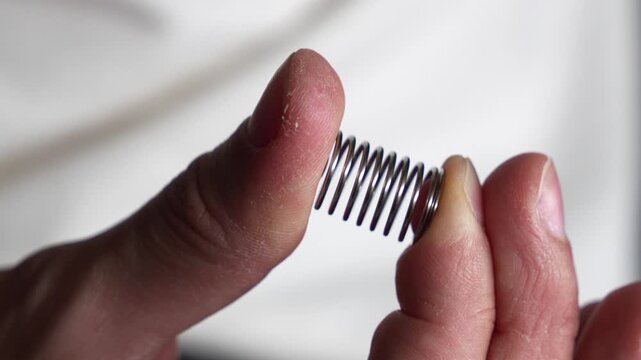 A man compresses a spring with his fingers.
A sturdy metal spring in the hands of a craftsman.
A man compresses a strong metal spring.
Spring, shock absorption, component, macro