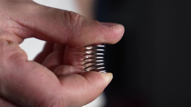 A man squeezes a tight, strong spring with his thumb.
A close-up of a metal spring in a man's hands.
Spring, metal, part, bending