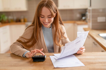 Woman calculating expenses in a cozy kitchen while reviewing bills on a wooden table in the morning light for better financial management