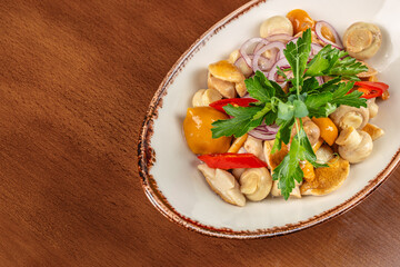 Marinated mushrooms with onions, peppers, and parsley in a white bowl on wooden background with copy space