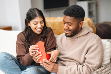 Couple shares joyful moment opening gift together in cozy living room during a relaxed weekend afternoon