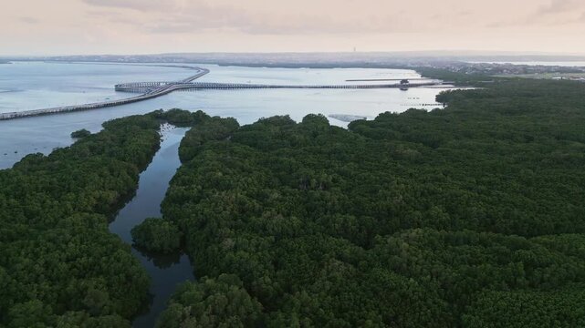 Aerial view of Bali Mandara Toll in the distance with a mangrove forest and winding river below during sunset capturing the serene tropical landscape and vibrant natural scenery