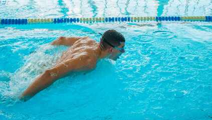 Professional Swimmer Performing Butterfly Stroke &ndash; Speed, Power and Determination. Swimming Competition &ndash; Athlete in Butterfly Style Training in Blue Water Pool