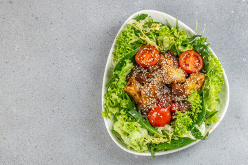 Fresh salad with lettuce, tomatoes, croutons, and sesame seeds on a gray background with copy space
