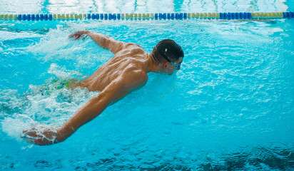 Professional Swimmer Performing Butterfly Stroke &ndash; Speed, Power and Determination. Swimming Competition &ndash; Athlete in Butterfly Style Training in Blue Water Pool