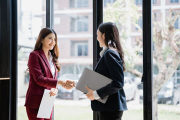 Obraz premium Two Asian businesswomen shaking hands after successfully signing a contract in a modern office by the window, embodying the spirit of collaboration and partnership in the corporate world