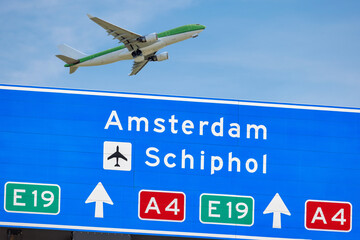 Dutch highway route sign to Amsterdam and Schiphol airport with passenger airplane in background