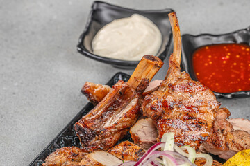 Grilled lamb chops with sauces and onions on a black plate with copy space