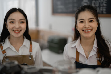 Two young, smiling Asian baristas welcoming customers in a vibrant coffee shop, preparing delicious beverages and serving fresh pastries with cheerful hospitality and friendly smiles