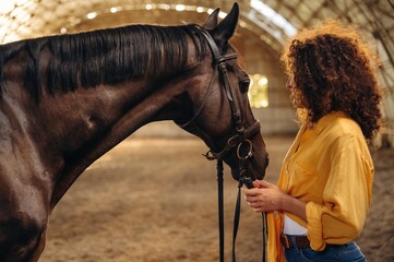 Beautiful young woman is with horse in hangar