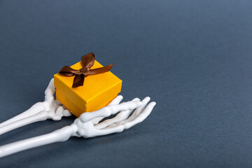 Halloween skeleton hands holding spooky gift box on dark background, copy space