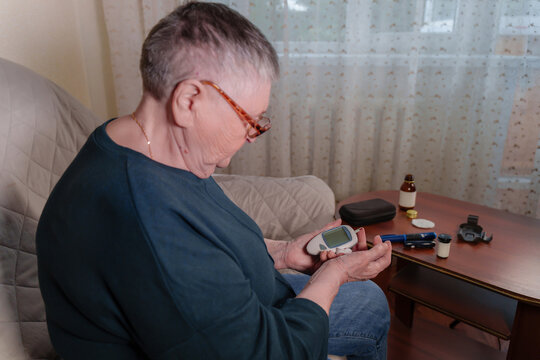 an older adult woman utilizing a handheld glucometer to test her blood sugar levels from the comfort of her own home.