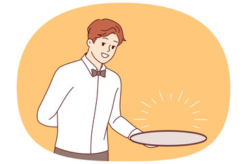 Man waiter with empty tray holds hand behind back, suggesting that you visit fabulous restaurant with delicious food. Guy waiter in formal wear with bow tie, smiling and looking at screen