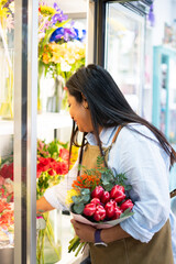Florist arranging bouquet of fresh flowers in flower shop refrigerator