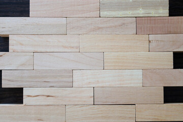 Wooden blocks, tightly stacked, form a rectangular wall on a dark background. The natural texture and shades of the wood are visible in the photo.