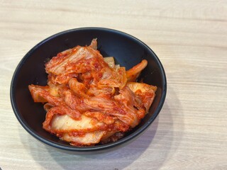 Authentic Korean Side Dish: Two Horizontal Shots of Spicy Fermented Napa Cabbage Kimchi (Baechu Kimchi) Served Generously in a Dark Matte Bowl on a Wooden Table.