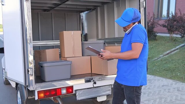 Close-up of a courier talking on the phone and picking up a box from a cargo van for delivery to a customer. Freight transport, goods delivery, online orders