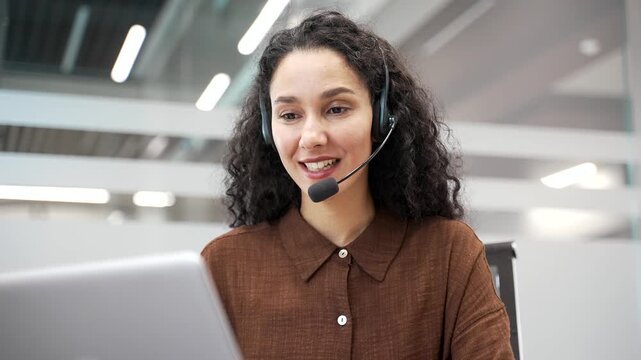 Female corporate operator in wireless headset working in customer support service on helpline telesale talking using laptop sitting in business office. Agent of call center advises client. Close up