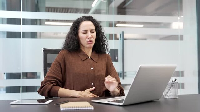 A sick businesswoman suffering from stomach pain while sitting at workplace in business office. Young female employee has poisoning, spasms, menstruation, gastritis, constipation or digestive problems