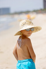 Mother and her son, cute blond boy, playing on the sea, hat, sunglasses, swimsuit, sun protection cream, sea and sand background. Concept: love, lifestyle, children, vacations