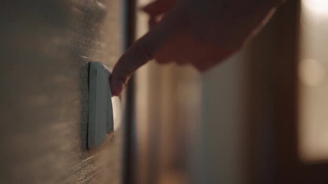Close-up of male finger activating light switch, symbolizing energy consumption, home automation, simple act of illuminating space in dark contemporary residential setting. Shooting in slow motion.
