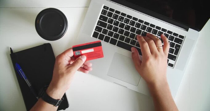 Man using laptop and holding credit card on desk with coffee cup and notebook. Concept of online shopping, ecommerce and digital payment.