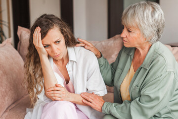 Worried aged mother embracing comforting sad grown up daughter with broken heart family sit on sofa