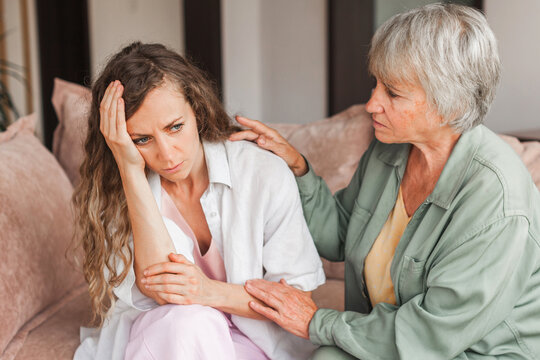 Worried aged mother embracing comforting sad grown up daughter with broken heart family sit on sofa