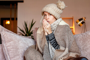 Woman warmly clothed and hat in a cold home sitting on couch