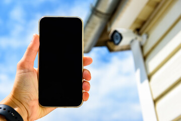 Security camera exterior on the wall of the house. Woman monitoring modern CCTV cameras on smartphone
