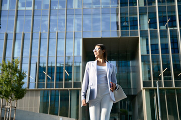 Portrait in action of indian or Latin confident successful ceo manager female businesswoman. Young hispanic woman in stylish business clothes walking outdoors at modern office building. Copy space