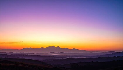 Obraz premium Panoramic Vista of Rolling Hills and Distant Cityscape at Sunset with Golden Sky and Purple Hues Dramatic Lighting Scenery Aerial Shot with Mountain Silhouette