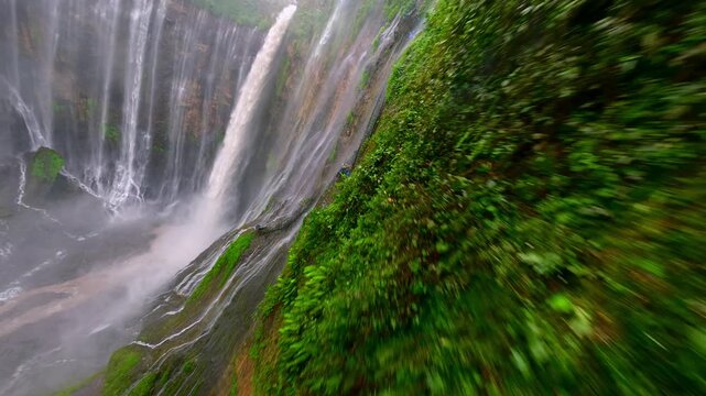 Cinematic FPV drone shot diving through the stunning multi-stream Tumpak Sewu waterfall, surrounded by lush rainforest cliffs in East Java, Indonesia.