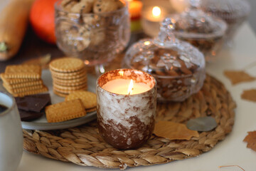 Lit candles, cookies, chocolate, nuts, tea, wine, pumpkins, books, reading glasses and autumn leaves on the table. Autumnal hygge at home. Selective focus.