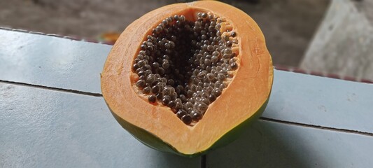 The image shows a ripe papaya fruit that is bright orange in color with a cavity containing many round black seeds, tightly packed together, contrasting with the soft flesh of the fruit.