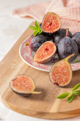 Ripe, fresh fig halves on a plate and a wooden board with stevia leaves and a pink napkin in a rustic setting