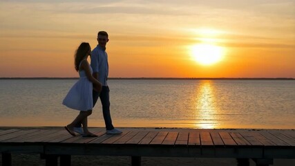 A couple is taking a leisurely stroll at sunset while enjoying their time on the pier together