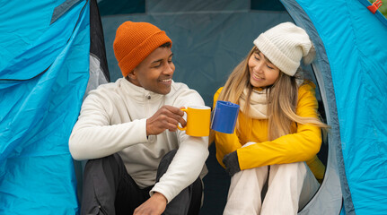 Smiling couple enjoying hot beverages inside their tent during a camping adventure