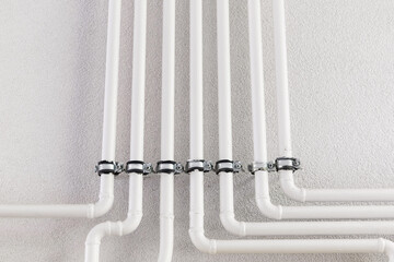 White plastic pipes connected to a white wall with sturdy metal clamps, forming a streamlined plumbing system for efficient water distribution