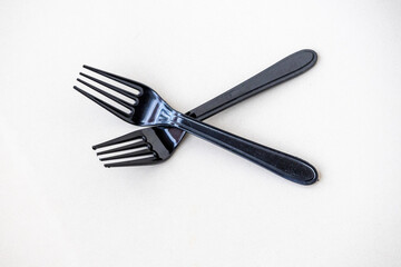 Fototapeta premium Two black plastic forks, isolated on a white background. These disposable utensils are a global environmental concern, contributing to plastic pollution and landfill waste.