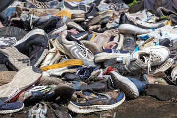 A large pile of dirty, old, and scattered footwear on a weathered concrete road, conveying themes...