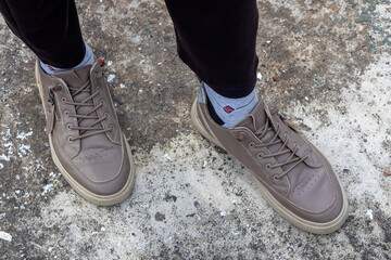 Stylish man's foot, wearing trendy laced shoes, standing on a textured concrete ground. A close-up shot focused on fashion, footwear, and urban style.