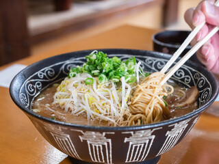 ネギともやしたっぷりのとんこつ醤油ラーメン。麺を箸あげしてる様子。