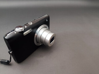 A black compact digital camera with an extended silver optical zoom lens, set against a dark, plain background.