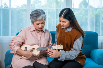 Senior Asian woman learning to play ukulele with young female family member at home