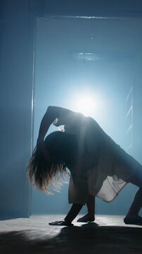 Insane contortionist woman in hospital gown bending into back arch and crawling with wild stare toward camera in dark corridor creepy horror Halloween cinematic slow motion scene