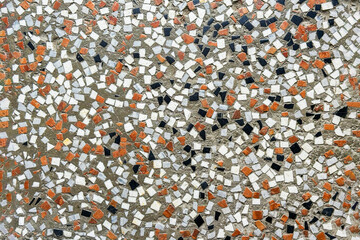 Fragment of an ancient decorative mosaic on the floor, close up. Broken ceramic tiles, brick and stone parts with cement grout wall decor. Abstract textured background.