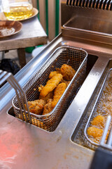 Close-up of deep fryer baskets with sizzling chicken nuggets, onion rings and french fries